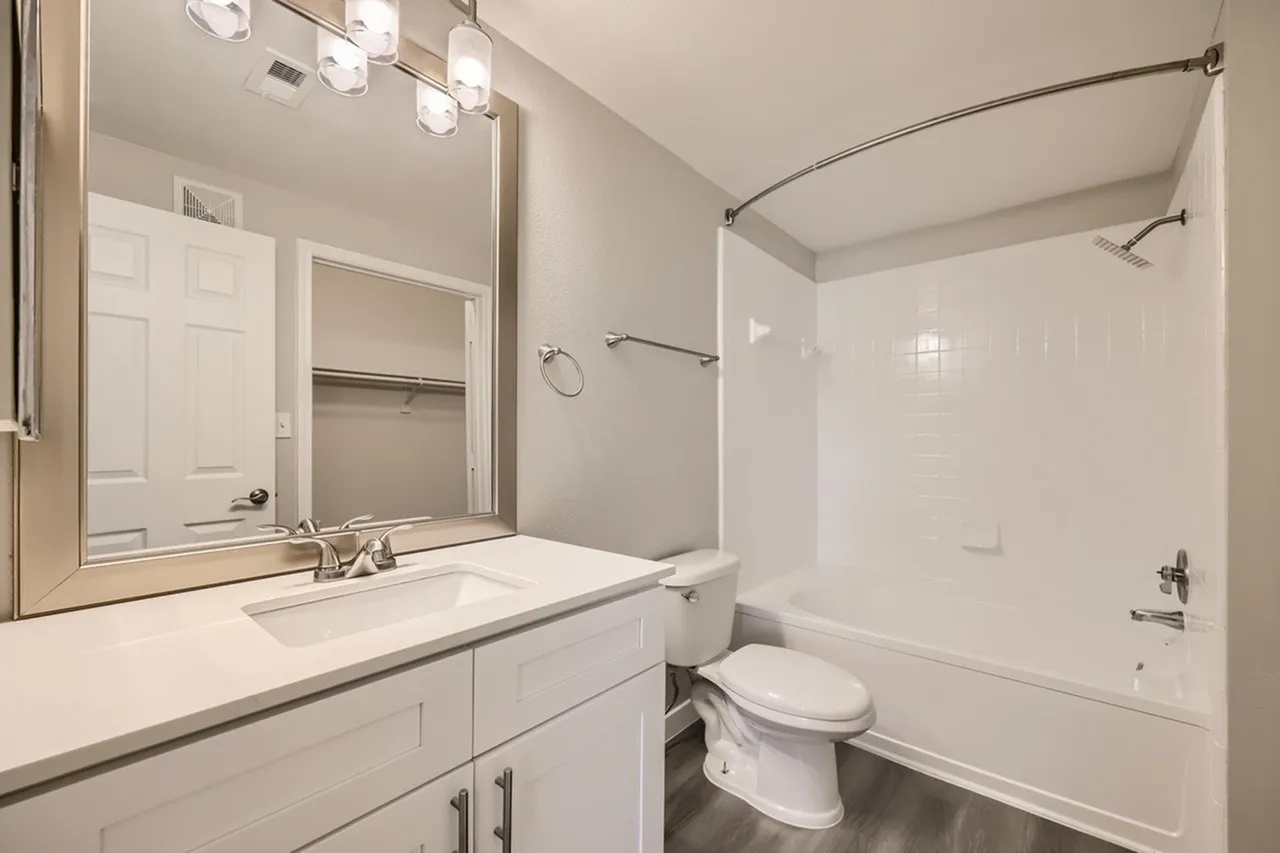 Primary bathroom, white vanity cabinetry, quartz countertops, chrome fixtures, bathtub with shower