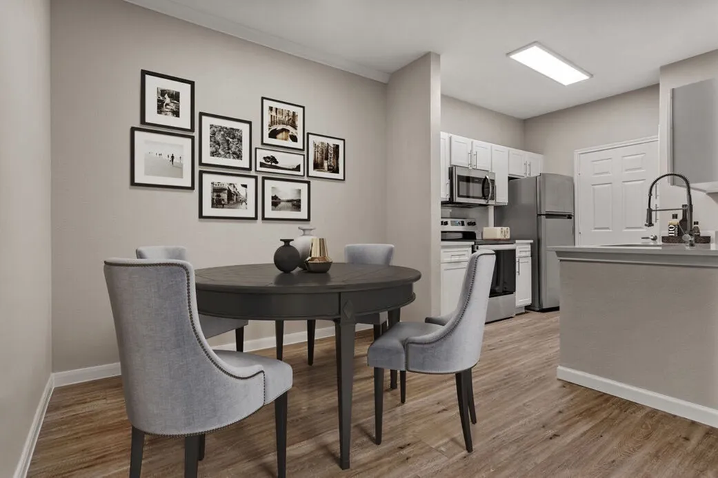 Dining area with round black table, gray upholstered chairs, wood-style plank flooring, stainless steel appliances, white cabinetry