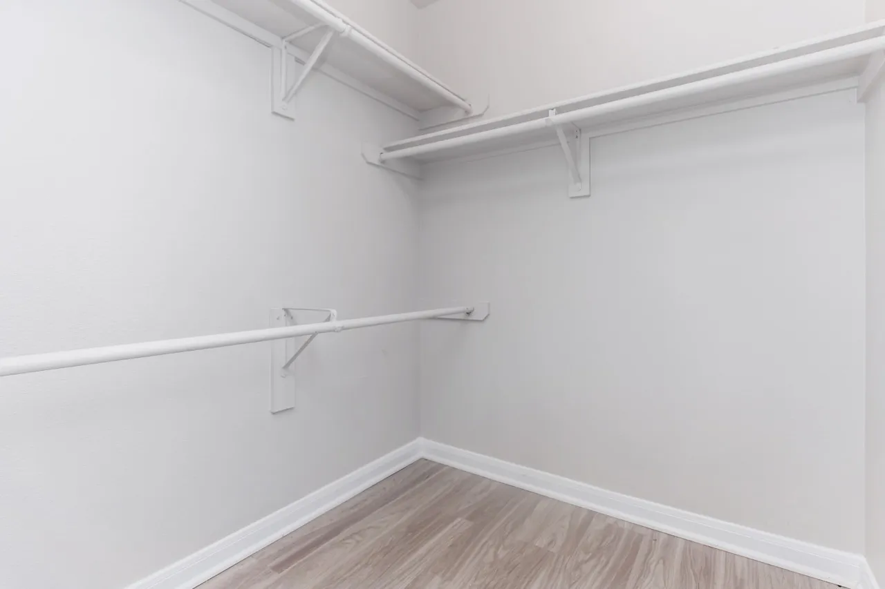 Walk-in closet, white walls, metal hanging rods, wood-style plank flooring