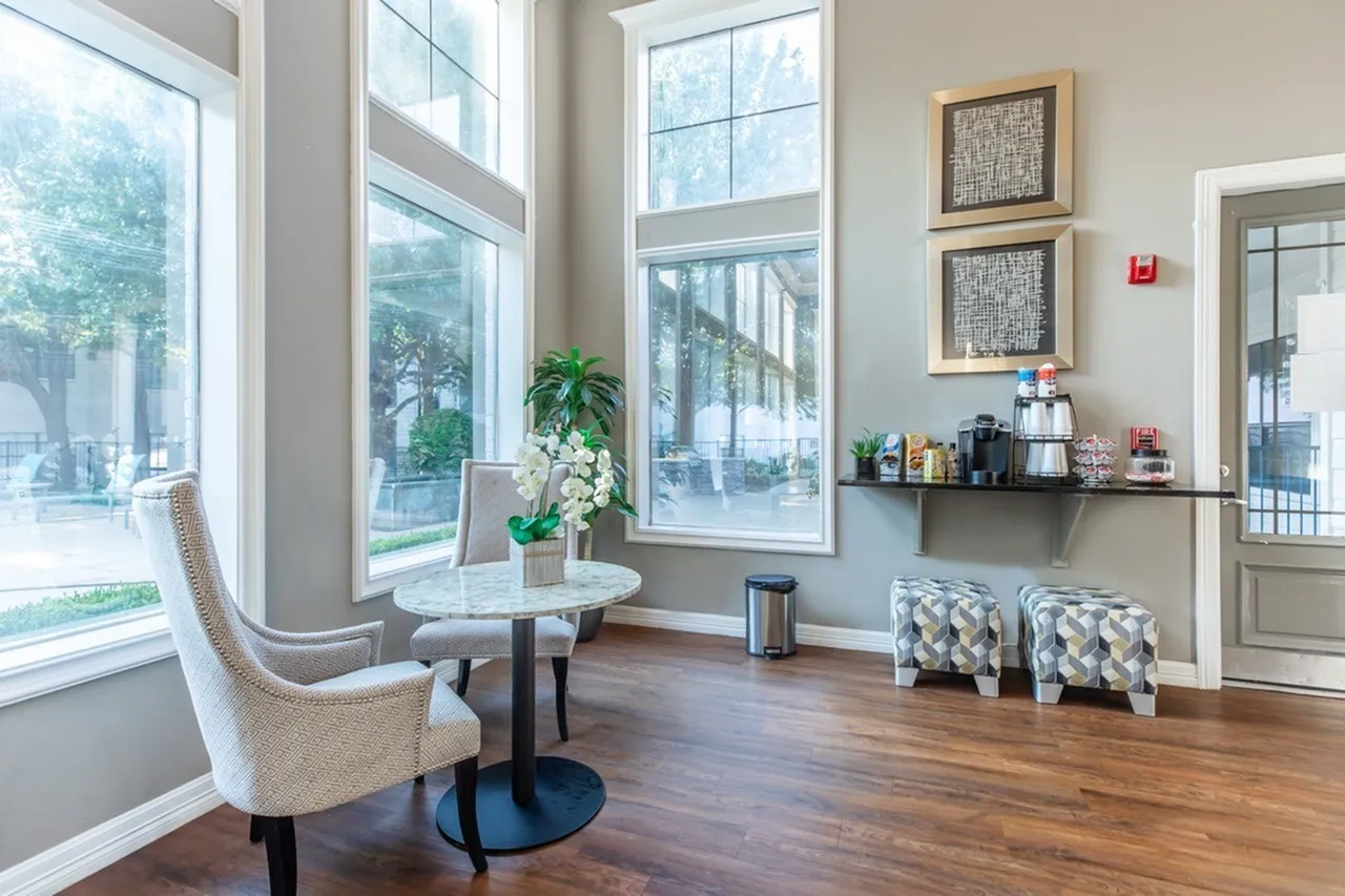 Lobby lounge, wood-style plank flooring, large windows, upholstered chair, potted plants