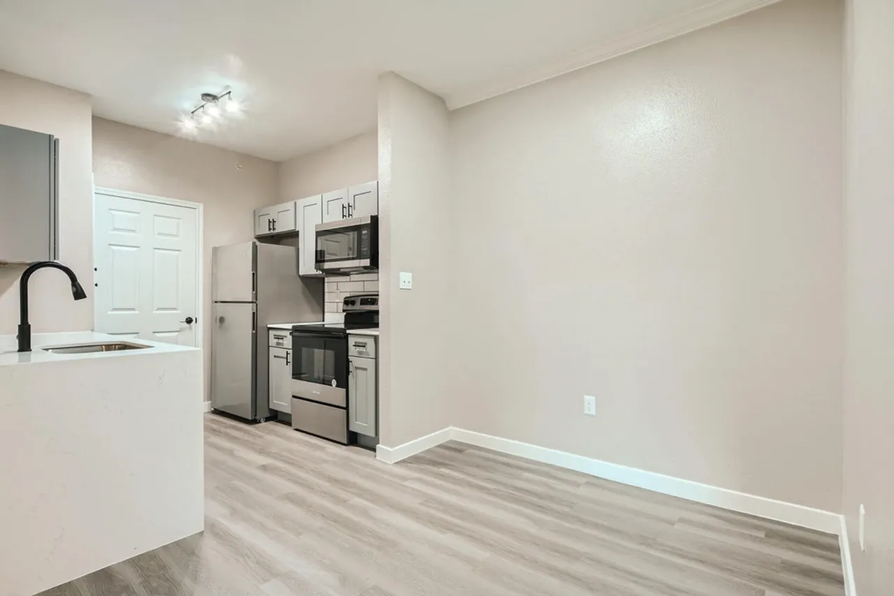Kitchen, white cabinetry, stainless appliances, wood-style plank flooring, open to dining space