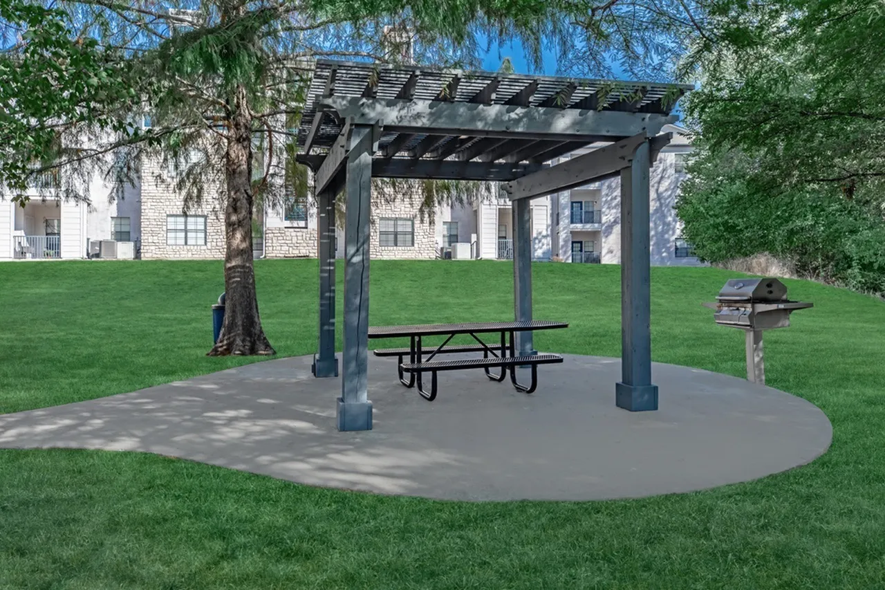 Pergola with picnic table, concrete pad, mature tree, green lawn, brick building