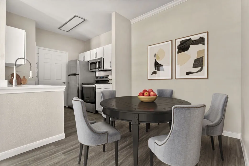 Dining room with black oval table, gray upholstered chairs, wood-style plank flooring, open kitchen with white cabinetry, stainless appliances