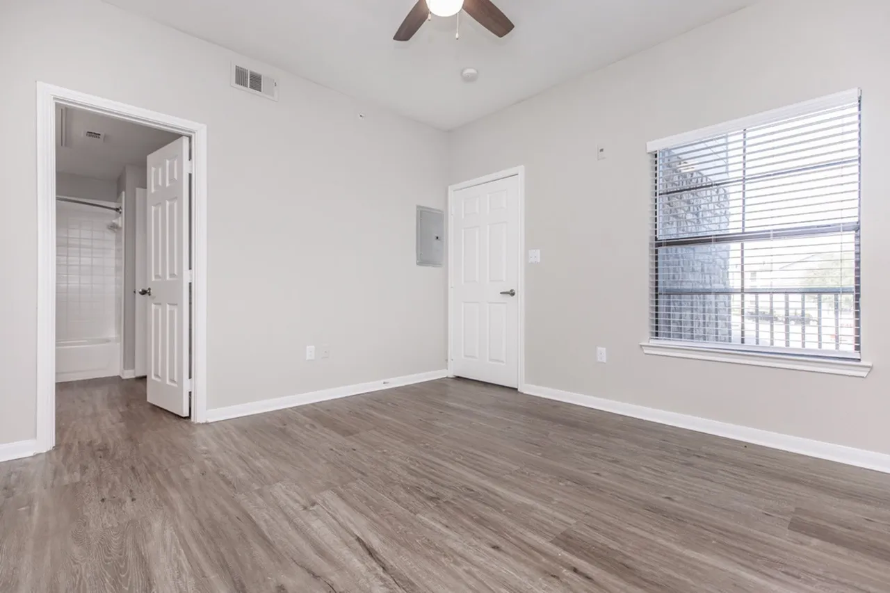 Primary bedroom, wood-style plank flooring, ceiling fan, window with blinds, ensuite bathroom