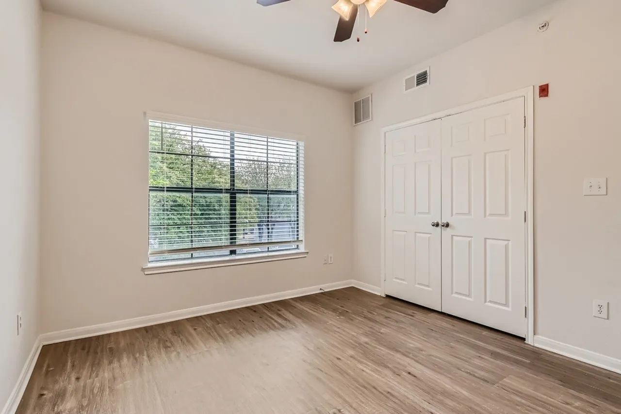 Bedroom, wood-style plank flooring, double closet doors, large window with shutters, ceiling fan