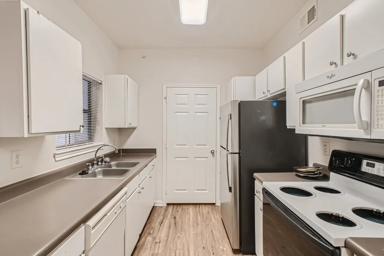 Galley kitchen, white cabinetry, stainless appliances, wood-style plank flooring