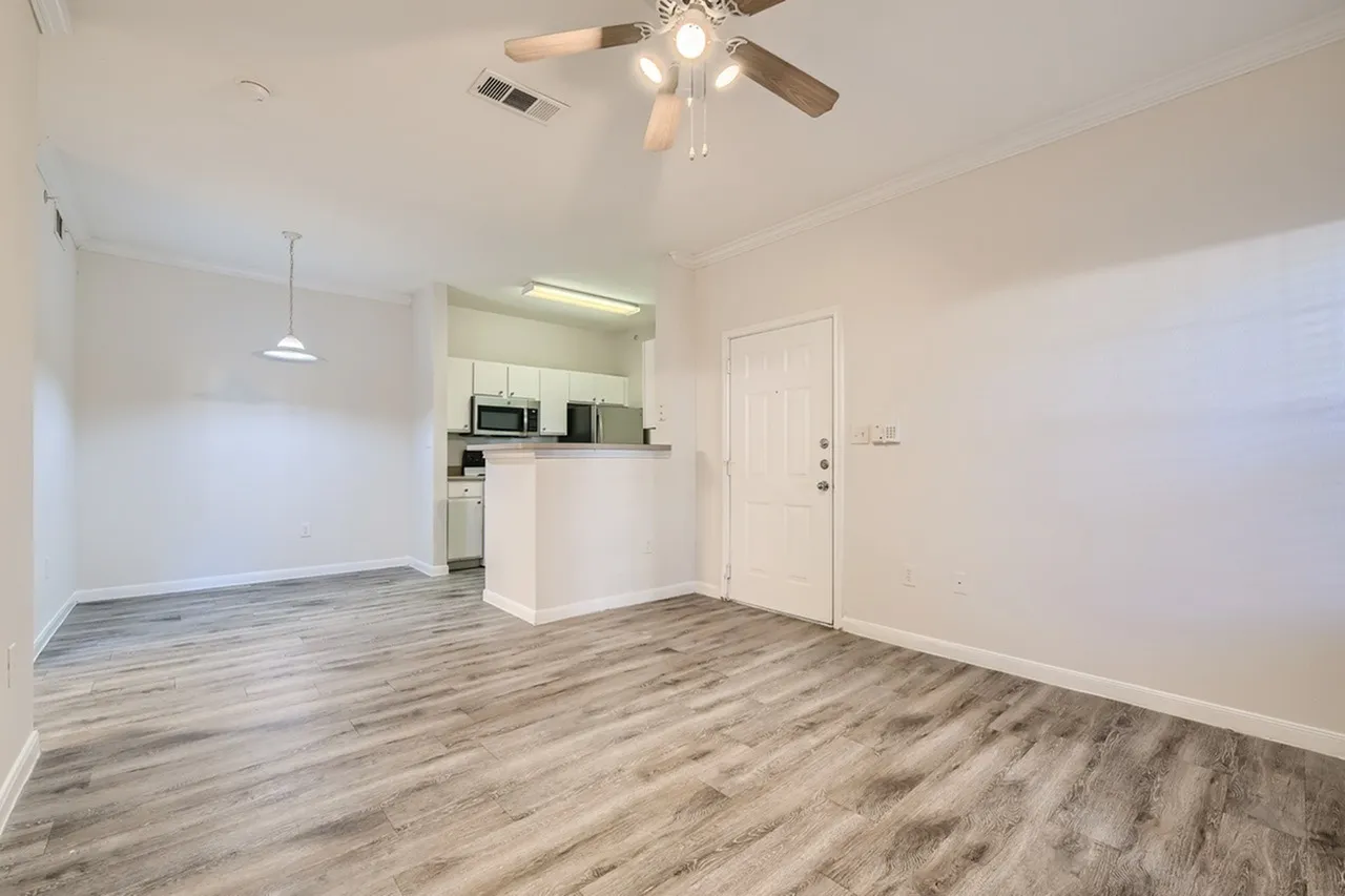Living room and kitchen area, wood-style plank flooring, white cabinetry, stainless appliances, ceiling fan
