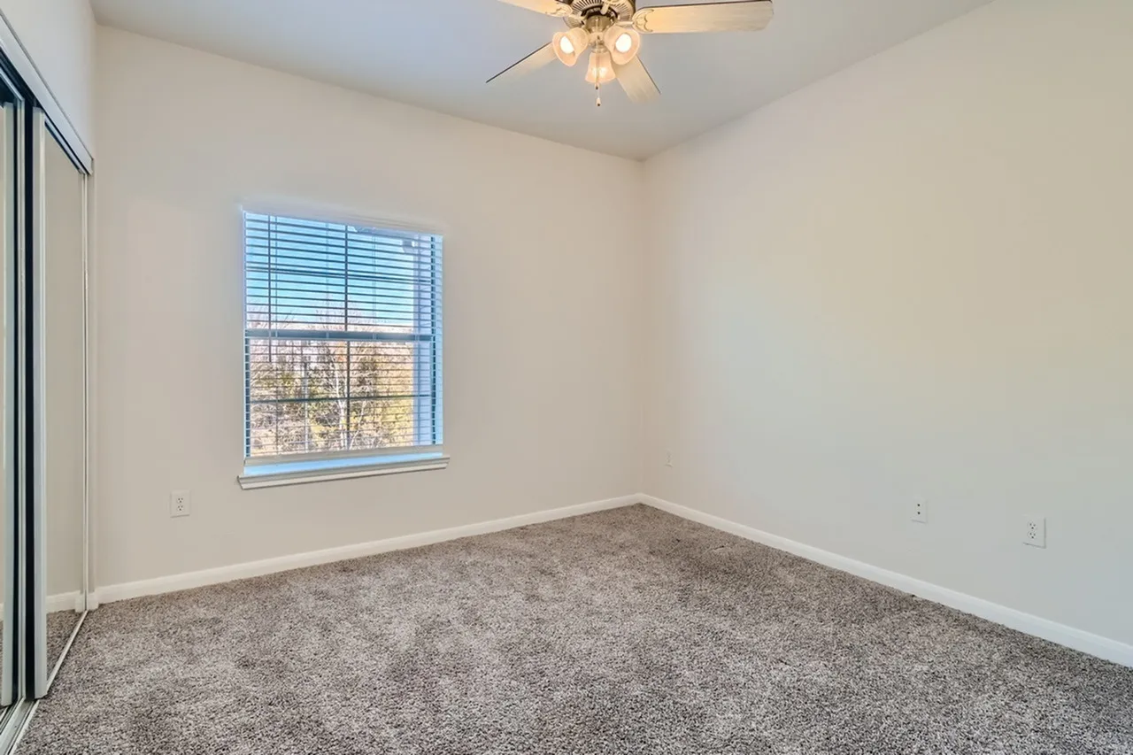 Bedroom, gray carpet flooring, ceiling fan, large window with blinds, white walls