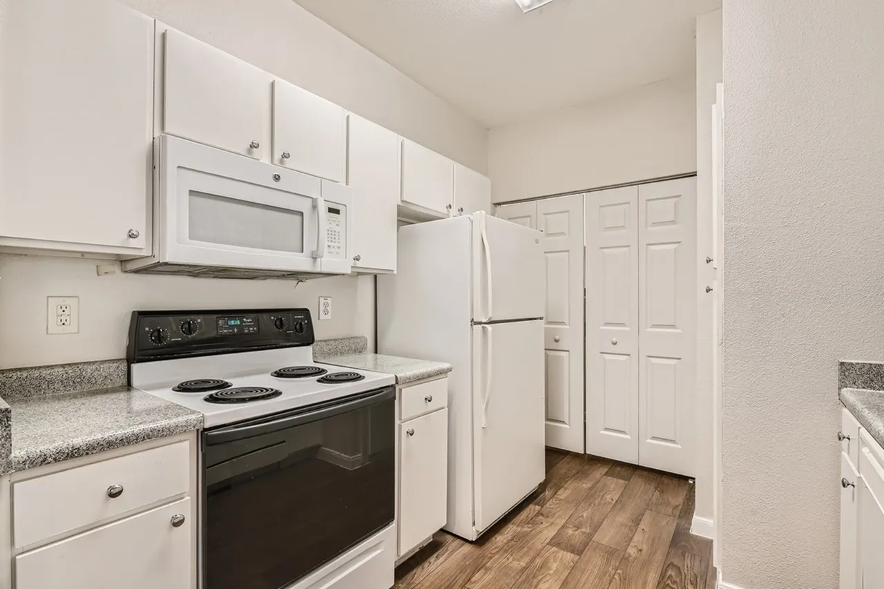 Kitchen, white cabinetry, granite countertops, black electric range, white refrigerator, microwave, wood-style plank flooring