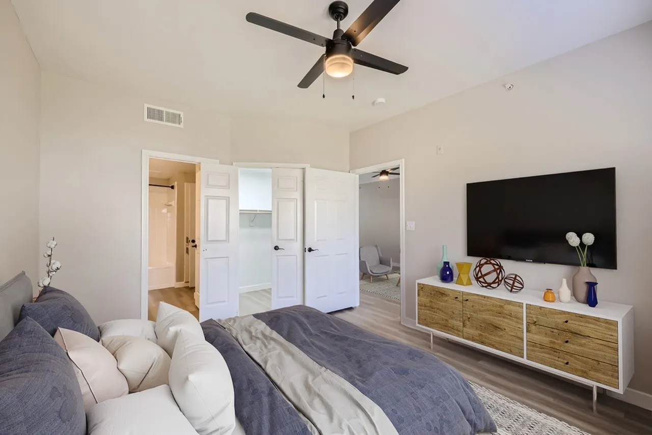 Primary bedroom, wood-style plank flooring, ceiling fan, flat-screen TV, wood dresser, walk-in closets