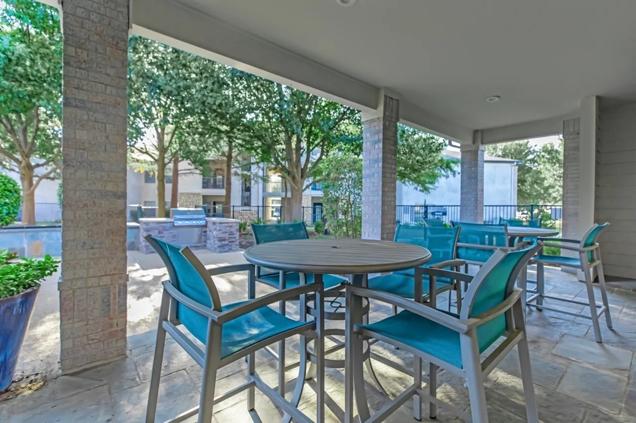 Covered patio, round dining table, teal chairs, stone columns, pool view