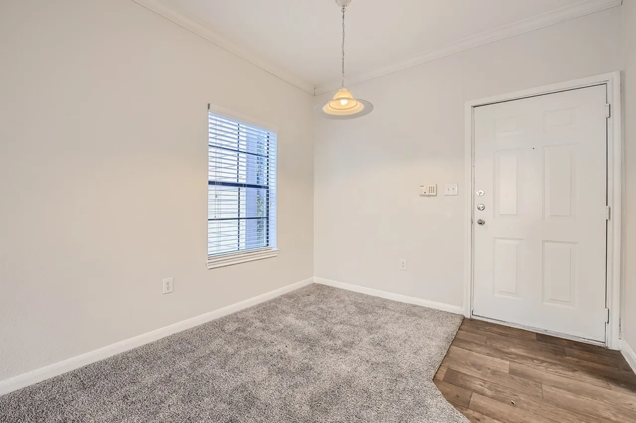 Dining area, wood-style plank flooring, gray carpeting, pendant light, white entry door