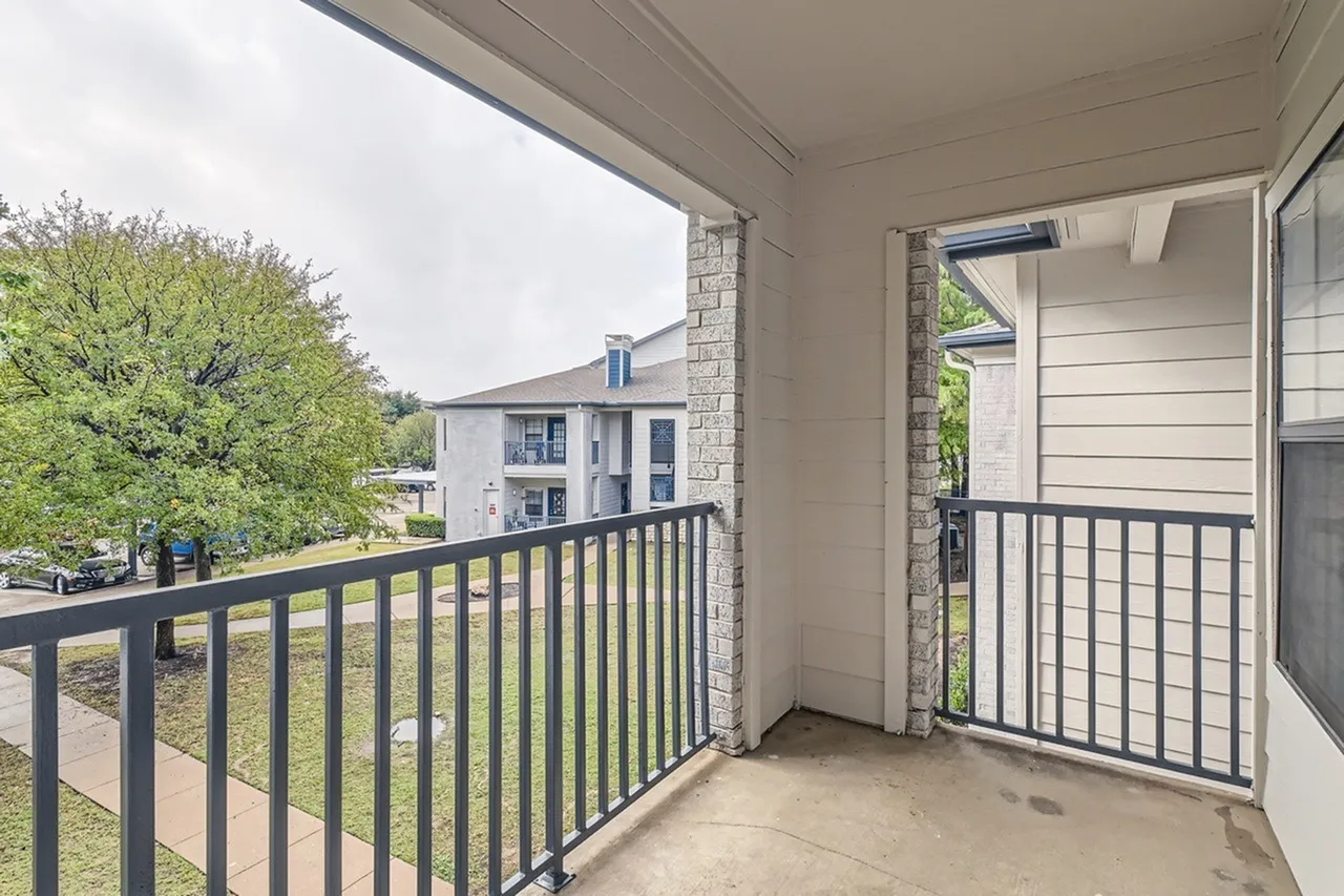 Balcony, black metal railing, concrete flooring, view of neighboring residential buildings and green landscaping