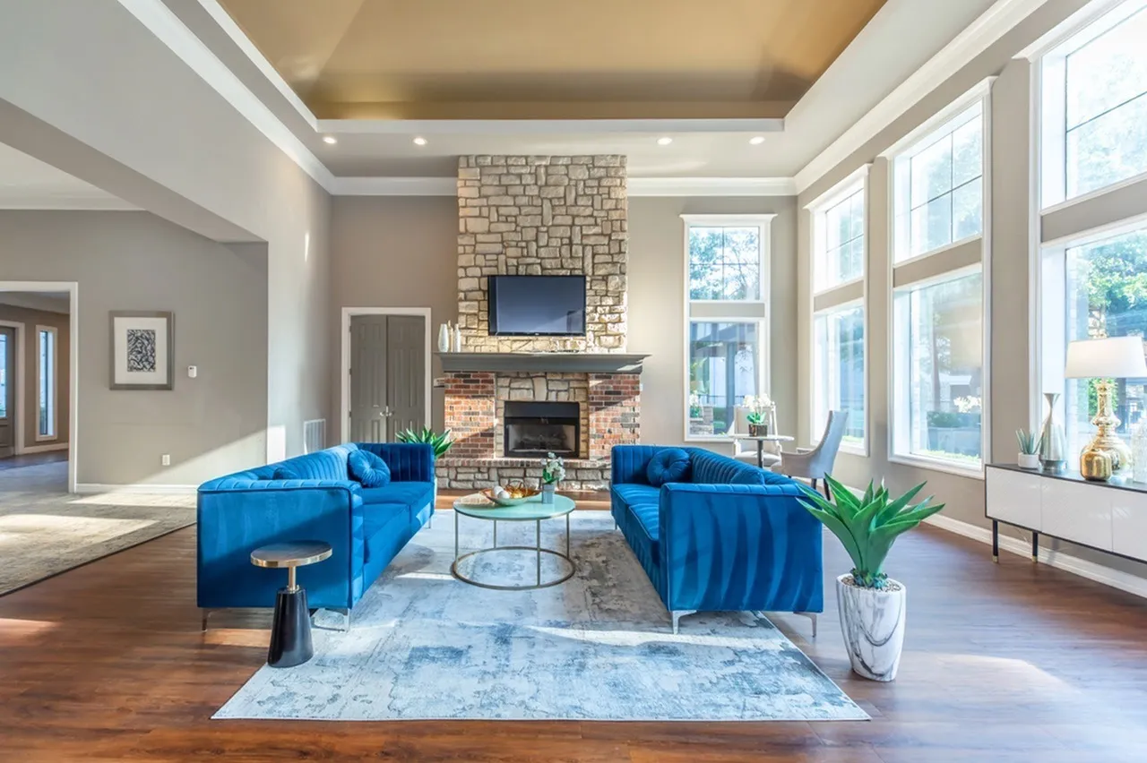 Living room, blue velvet sofas, brick fireplace with TV, wood-style plank flooring, large windows