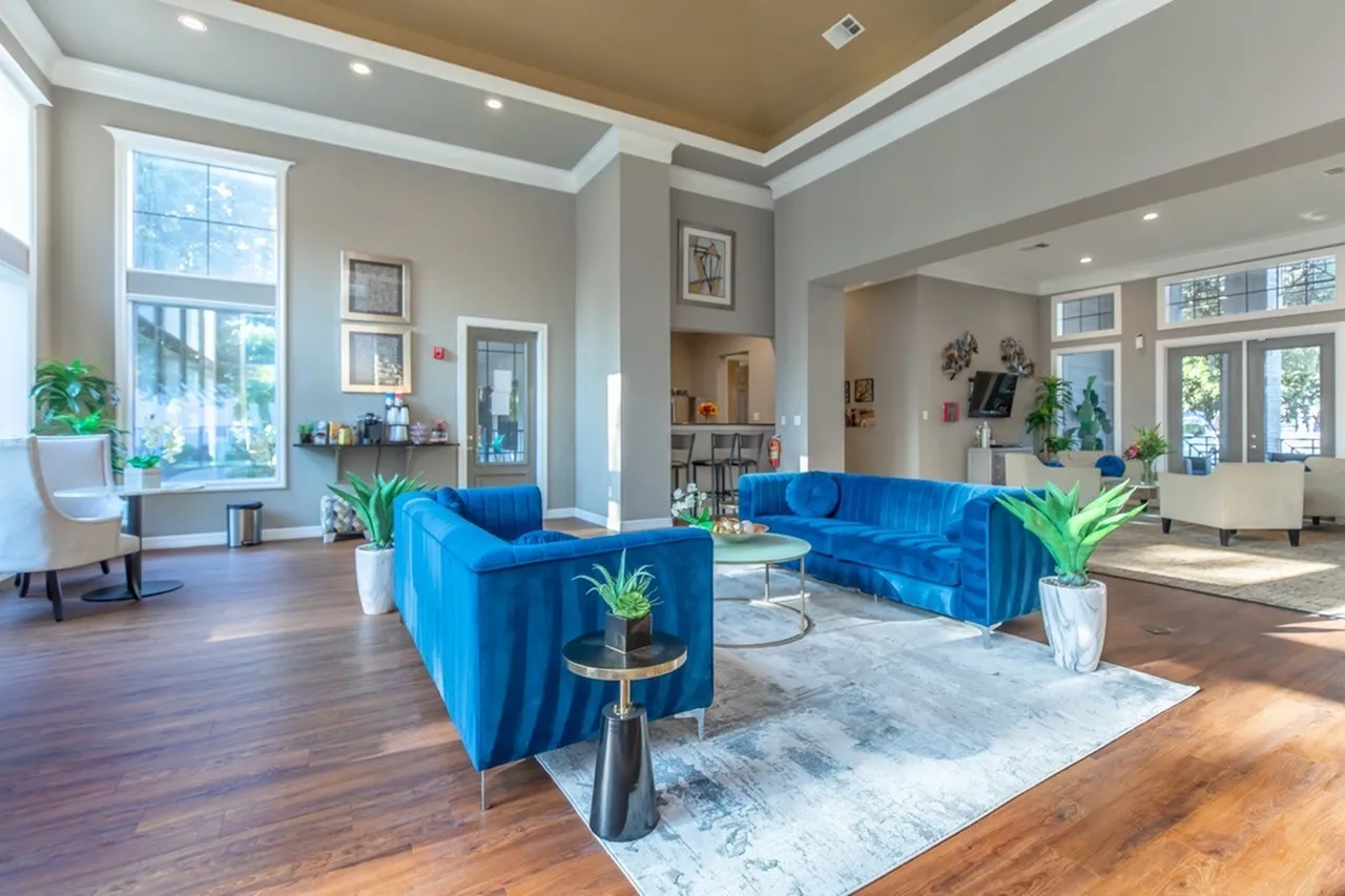 Lobby seating area, bright blue upholstered sofas, wood-style plank flooring, large windows, potted plants