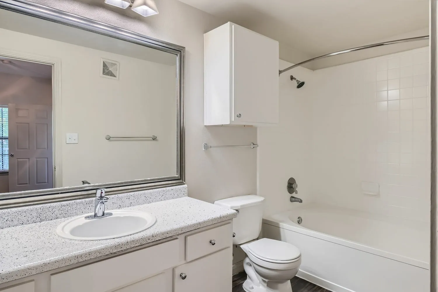Primary bathroom, speckled quartz countertops, white vanity cabinetry, large framed mirror, ceramic tile surround