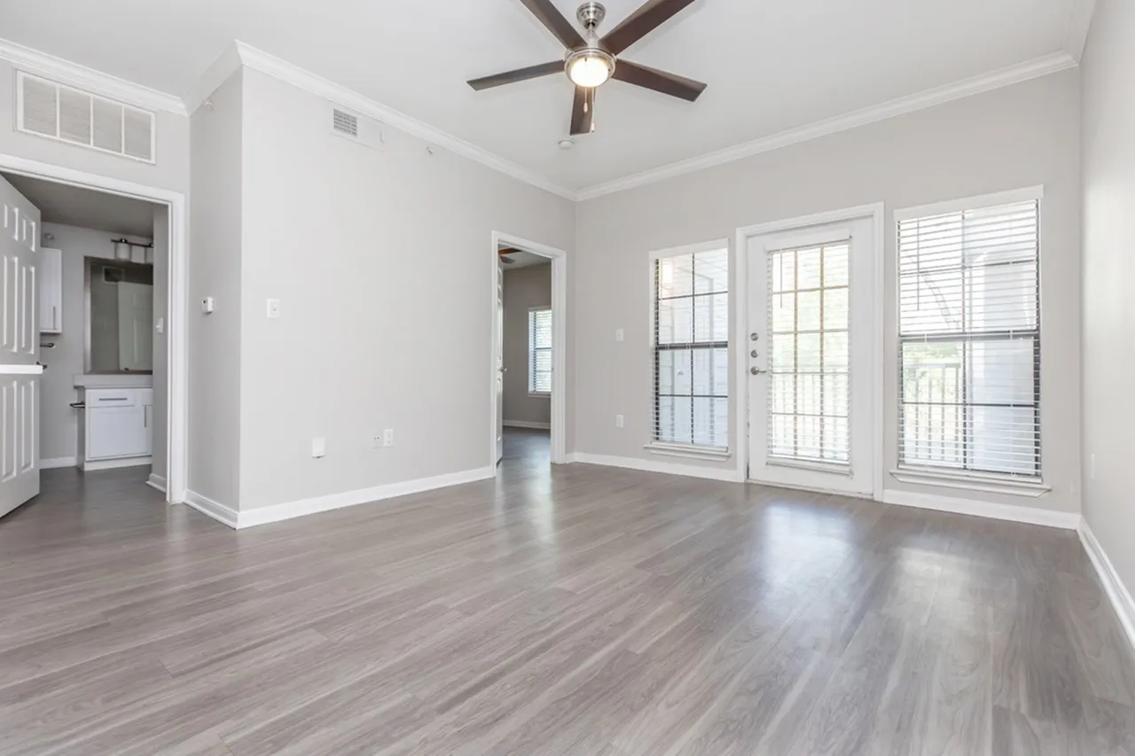 Living room with wood-style plank flooring, ceiling fan, glass patio doors, shutters