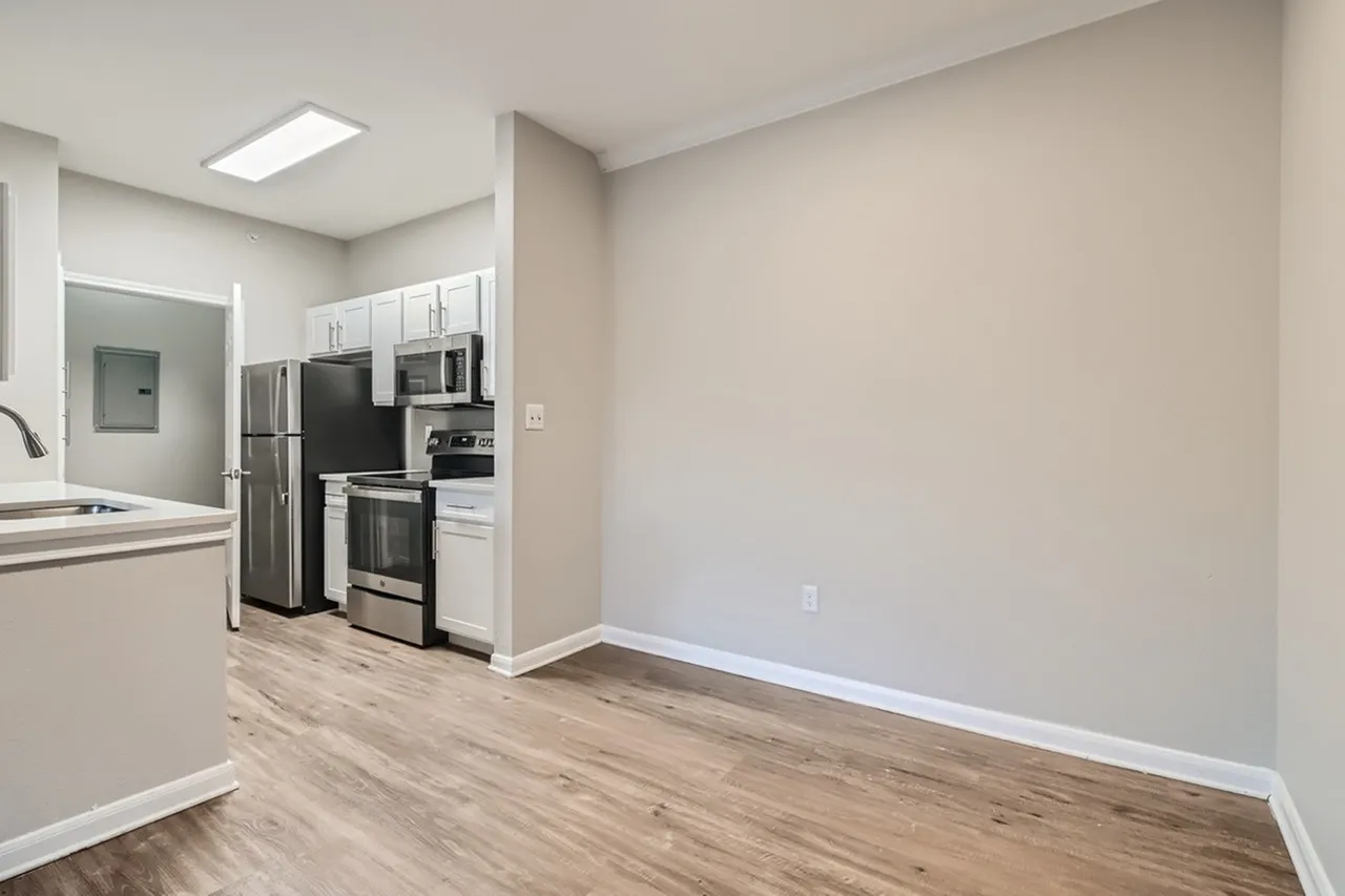 Kitchen with stainless steel appliances, white cabinetry, wood-style plank flooring, open dining space