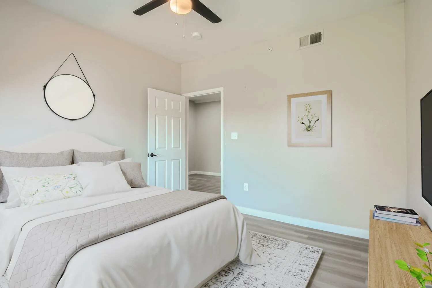 Primary bedroom, wood-style plank flooring, ceiling fan, round mirror, ensuite entry
