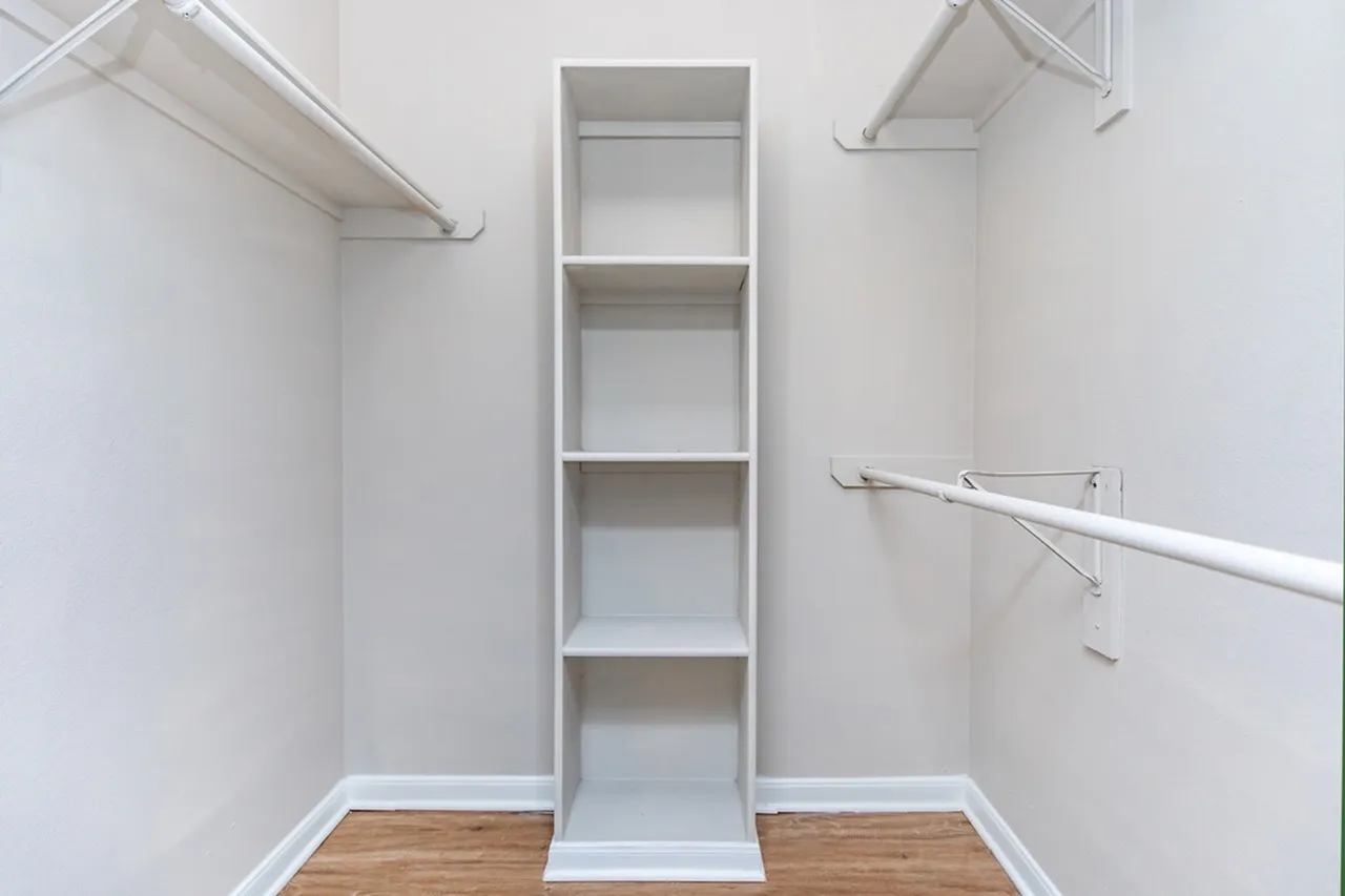 Walk-in closet, white built-in shelving, wood-style plank flooring, clothing rods, white walls