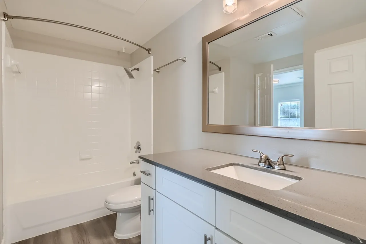 Primary bathroom, white vanity cabinetry, quartz countertop, framed mirror, wood-style plank flooring