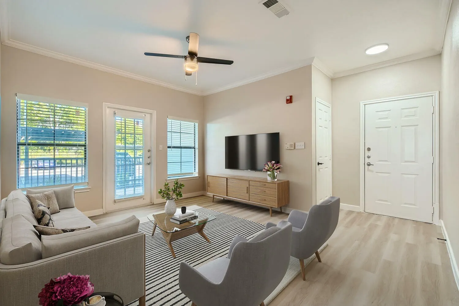 Living room, wood-style plank flooring, ceiling fan, wall-mounted TV, large windows with water view