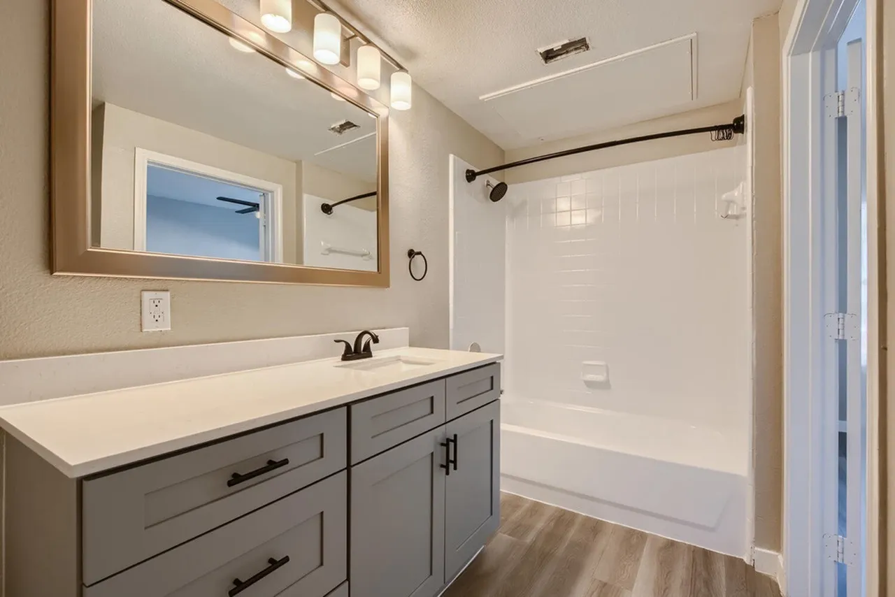 Primary bathroom, gray vanity cabinetry, white quartz countertops, framed mirror, walk-in shower