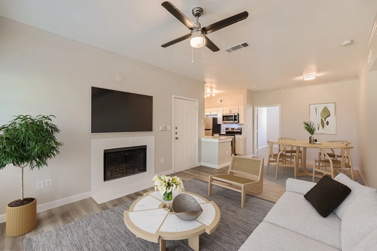 Living room with wood-style plank flooring, ceiling fan, fireplace, TV, sofa, armchair