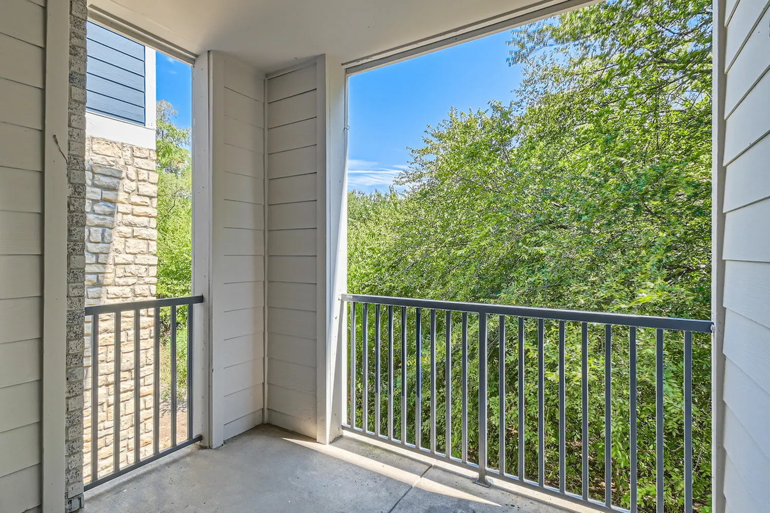 Balcony, metal railing, dual glass doors, tree canopy view, bright natural light