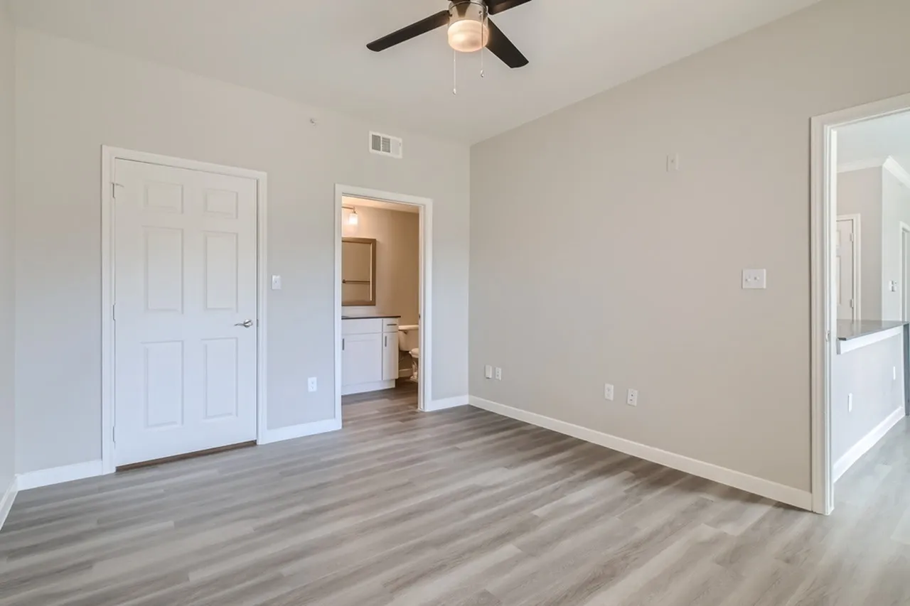 Primary bedroom, wood-style plank flooring, ceiling fan, ensuite access, white doors