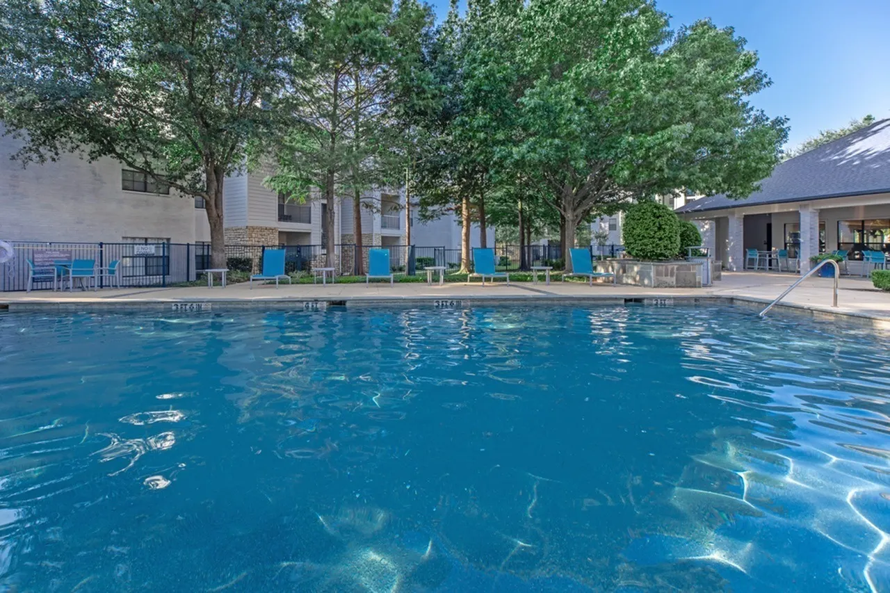 Swimming pool, blue water, lounge chairs, mature trees, residential buildings