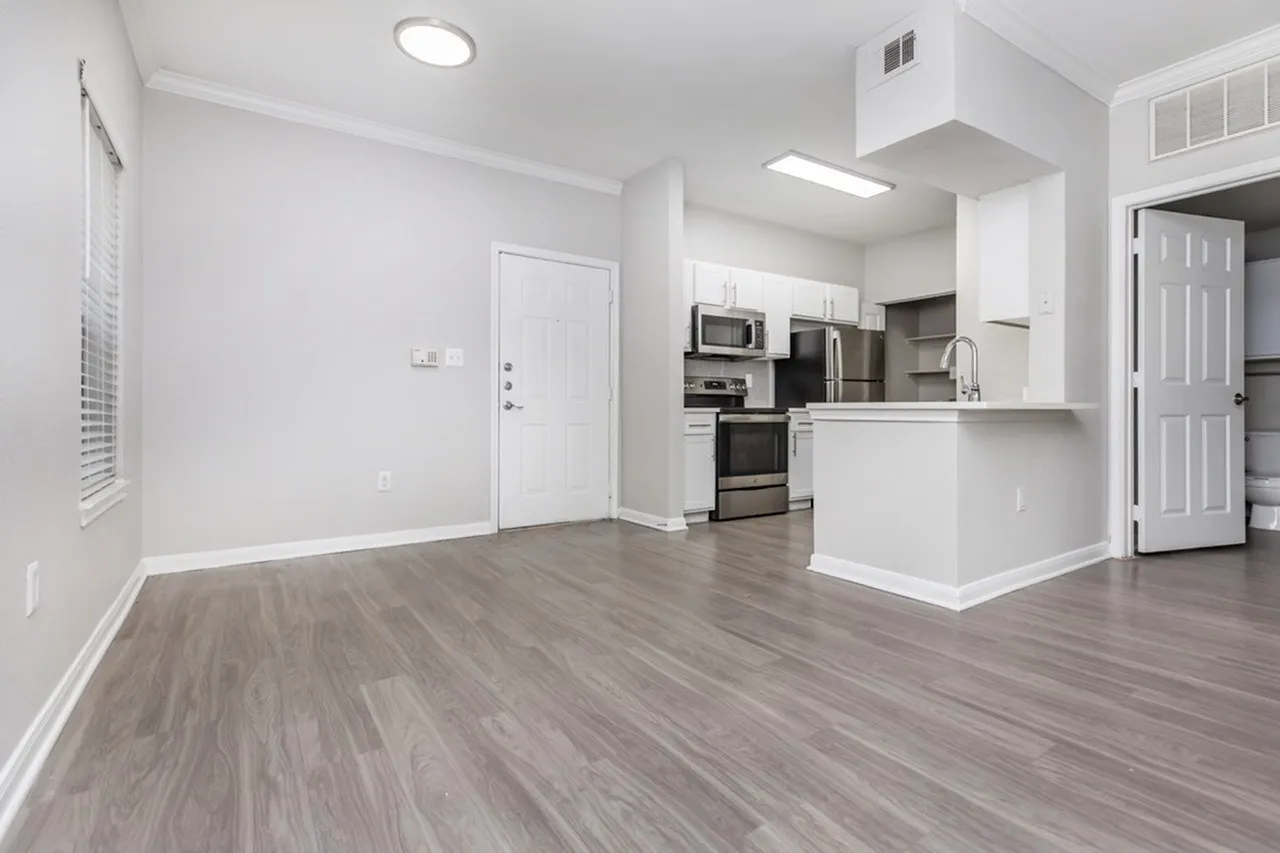 Open concept kitchen and living room, wood-style plank flooring, white cabinetry, stainless appliances, quartz countertops