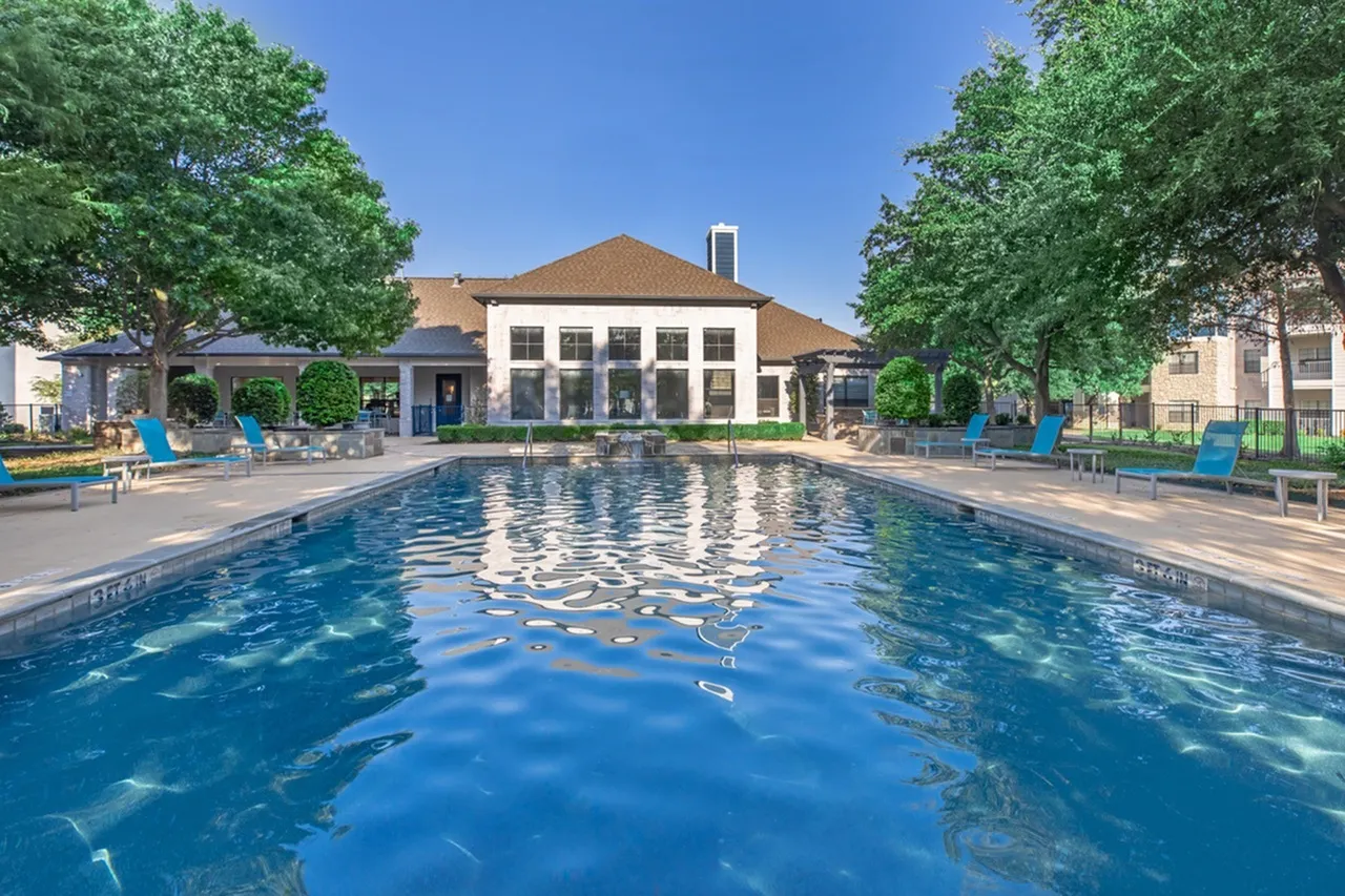 Outdoor swimming pool, brick clubhouse with white columns, lounge seating, mature trees