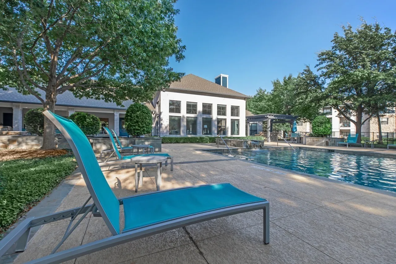 Pool area with blue lounge chairs, resort-style seating, mature trees, clubhouse