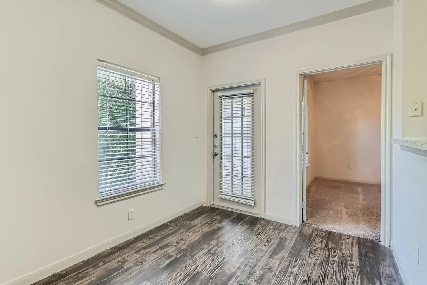 Living room with wood-style plank flooring, shuttered windows, entry door, cream walls