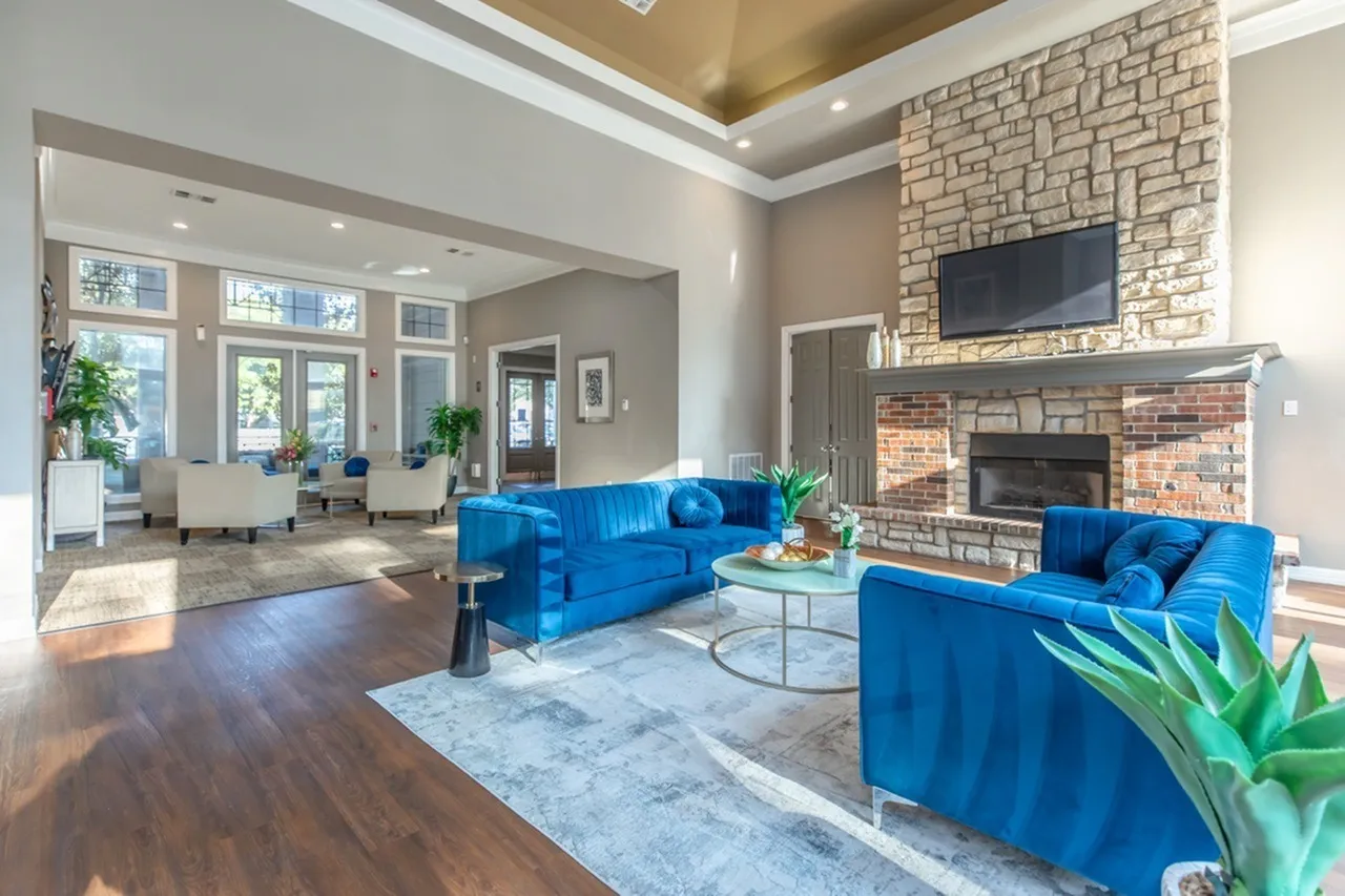 Living room, wood-style plank flooring, blue velvet sofa, brick fireplace with TV, natural light