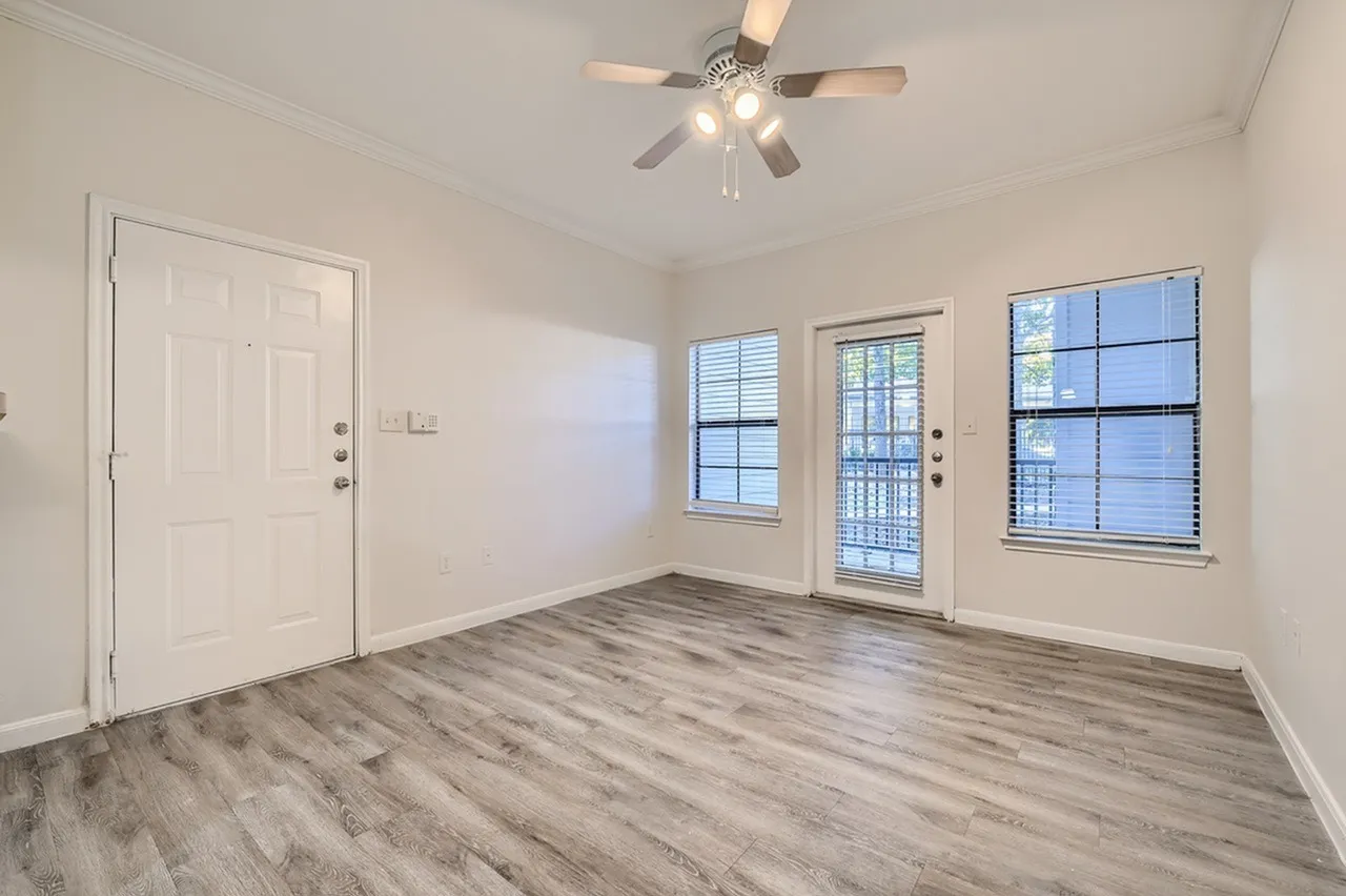Living room, wood-style plank flooring, ceiling fan with lights, entry door, windows with blinds