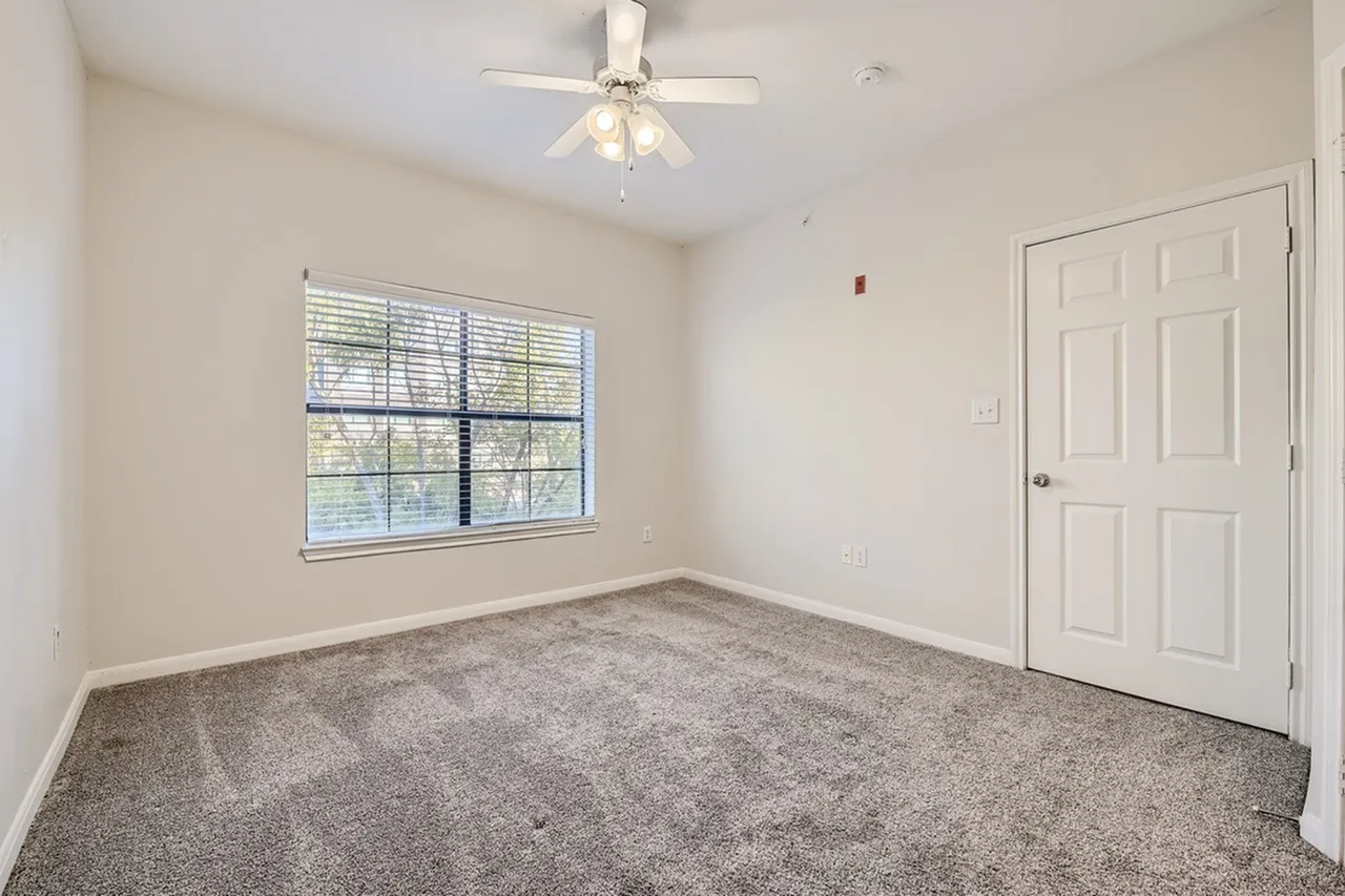 Bedroom, gray carpet flooring, ceiling fan with light fixture, large window, white six-panel door