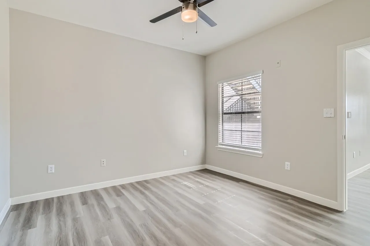 Bedroom, wood-style plank flooring, ceiling fan with light fixture, window with blinds, neutral walls