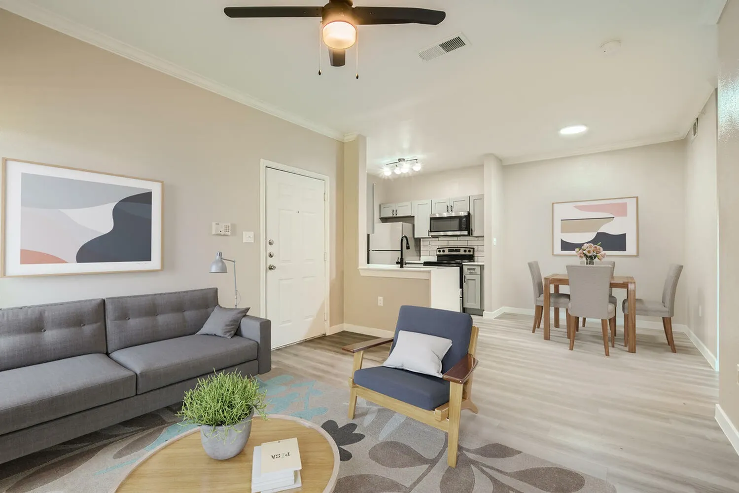 Living room with gray sofa, wood-style plank flooring, ceiling fan, dining area visible