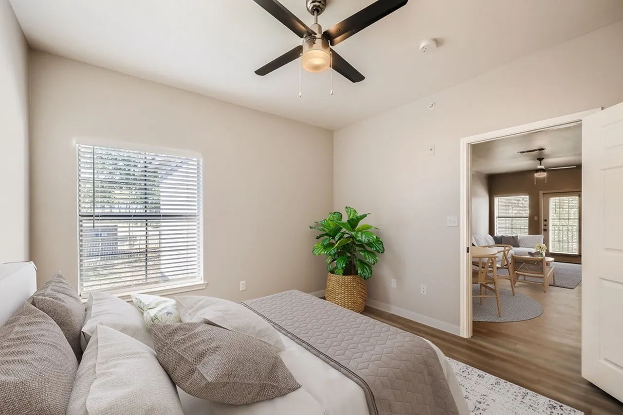 Primary bedroom, wood-style plank flooring, ceiling fan, green potted plant, French doors