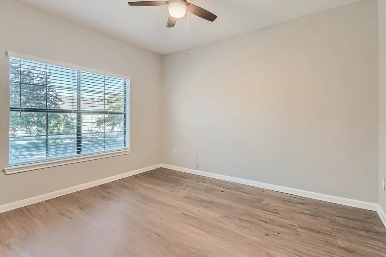 Bedroom, wood-style plank flooring, ceiling fan, large window with shutters, neutral walls