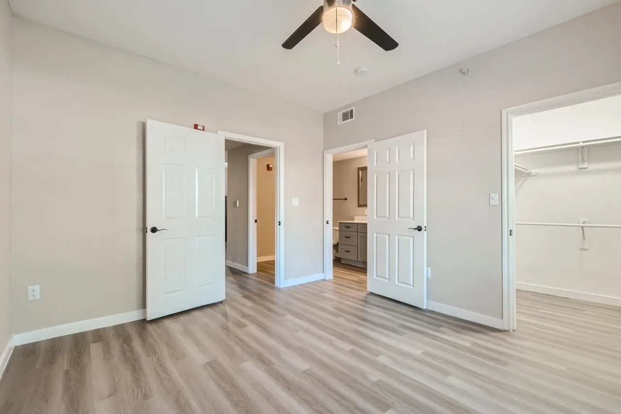 Primary bedroom, wood-style plank flooring, ceiling fan, multiple door entries to closet and bathroom