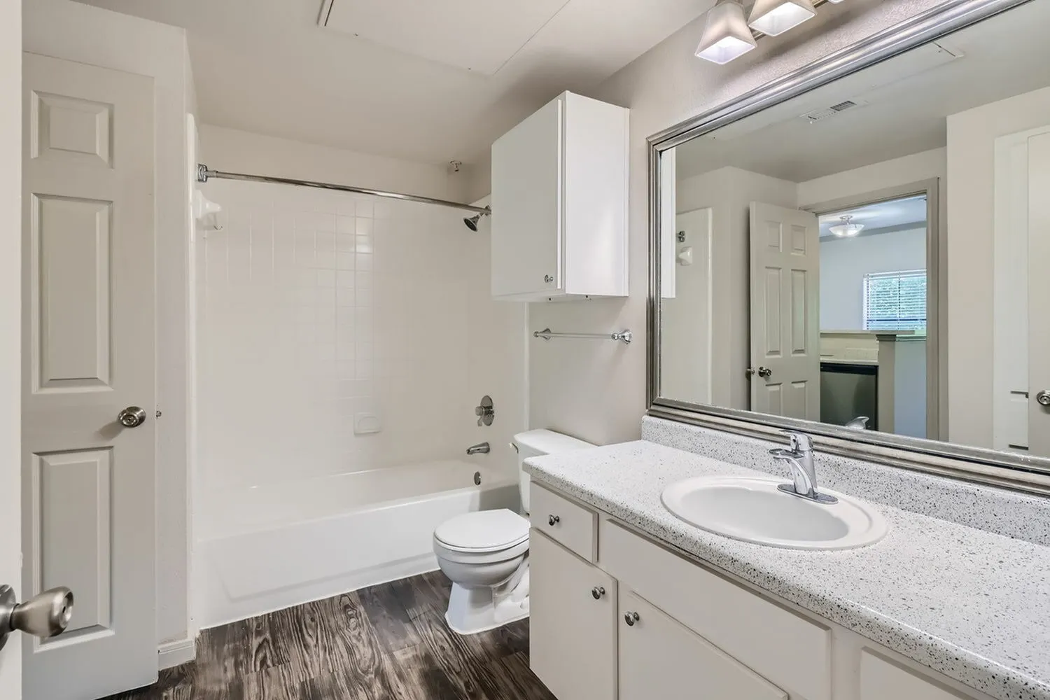 Primary bathroom, white vanity with quartz countertops, mirror, ceramic sink, wood-style plank flooring