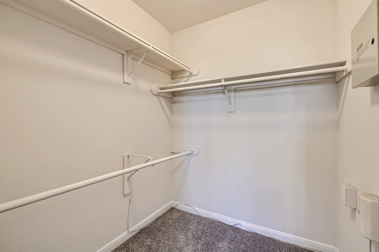 Walk-in closet, metal clothing rods, gray carpeting, white walls
