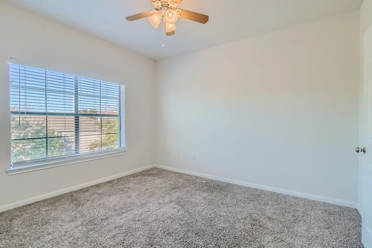 Bedroom, gray carpet flooring, ceiling fan, large window with shutters, white walls