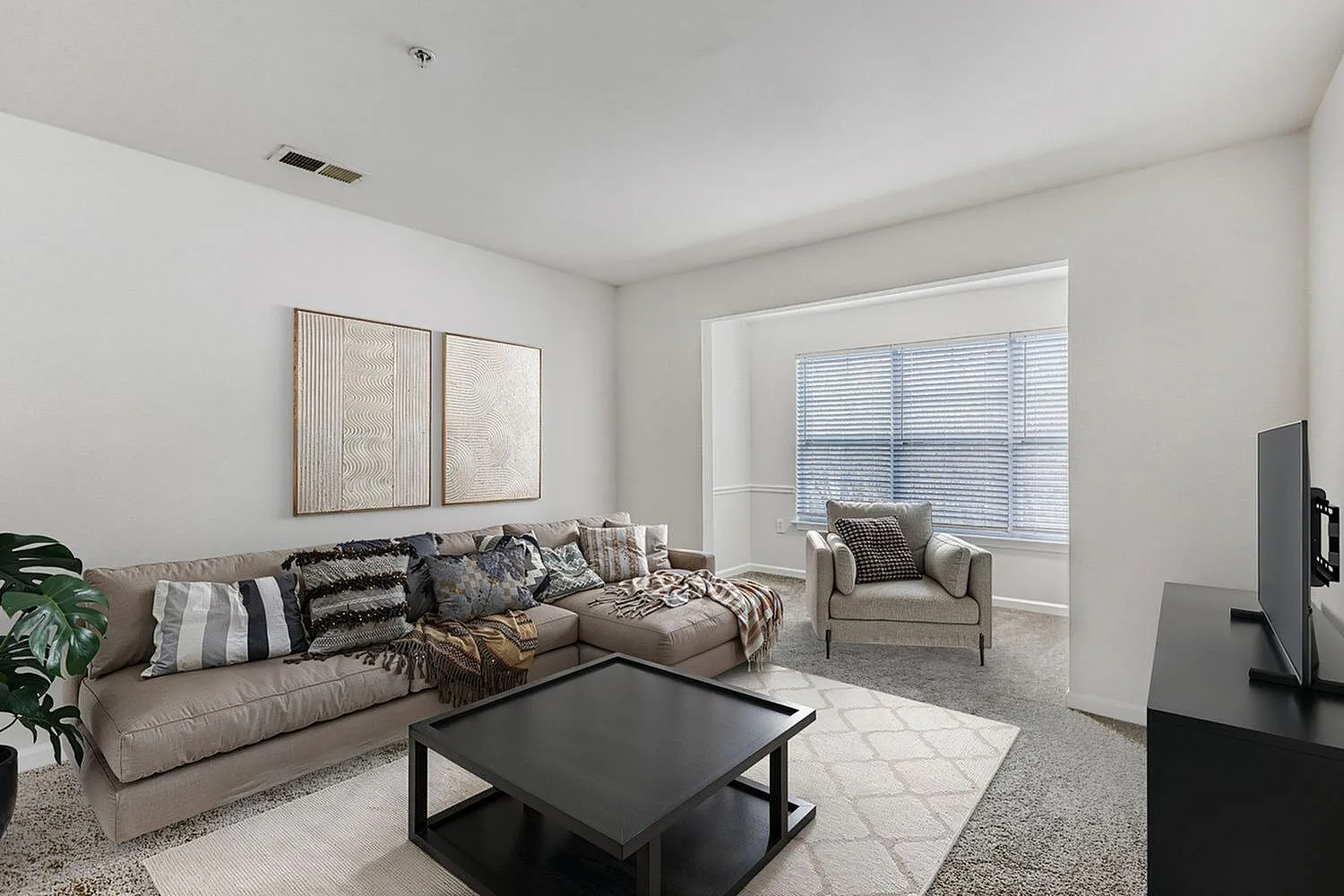 Living room, taupe sectional sofa, black coffee table, wood-style plank flooring, white blinds