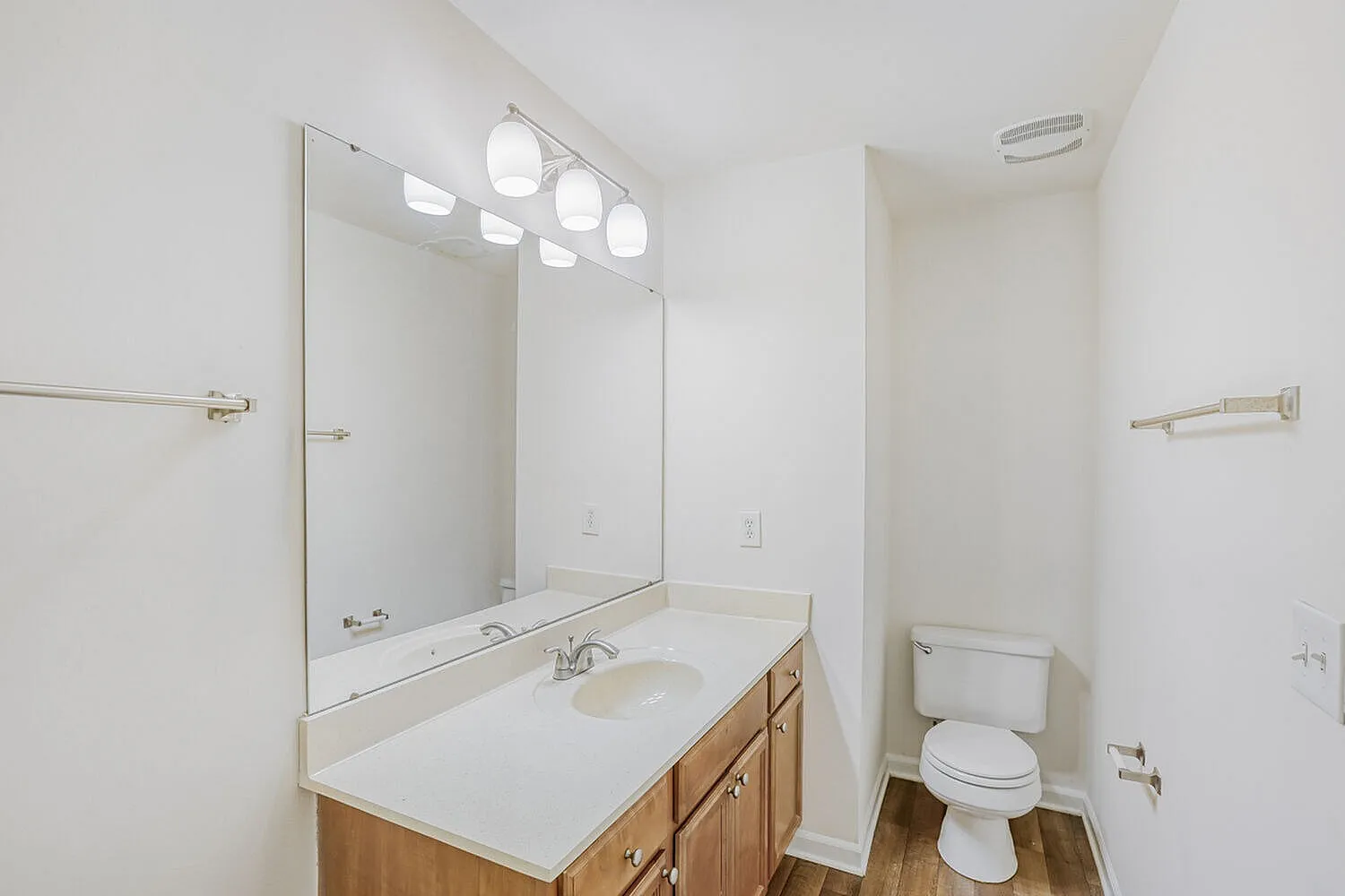 Primary bathroom, wood-style vanity cabinet, white quartz countertop, large mirror, chrome fixtures