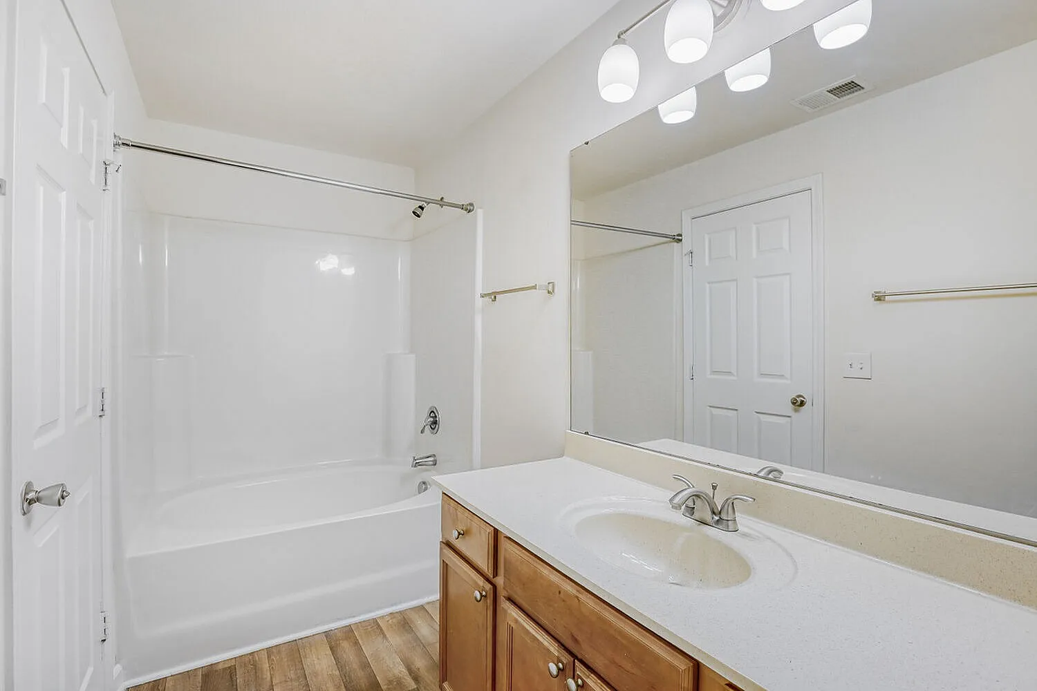 Primary bathroom, wood-style plank flooring, wood vanity cabinetry, white countertop, white ceramic sink, large mirror