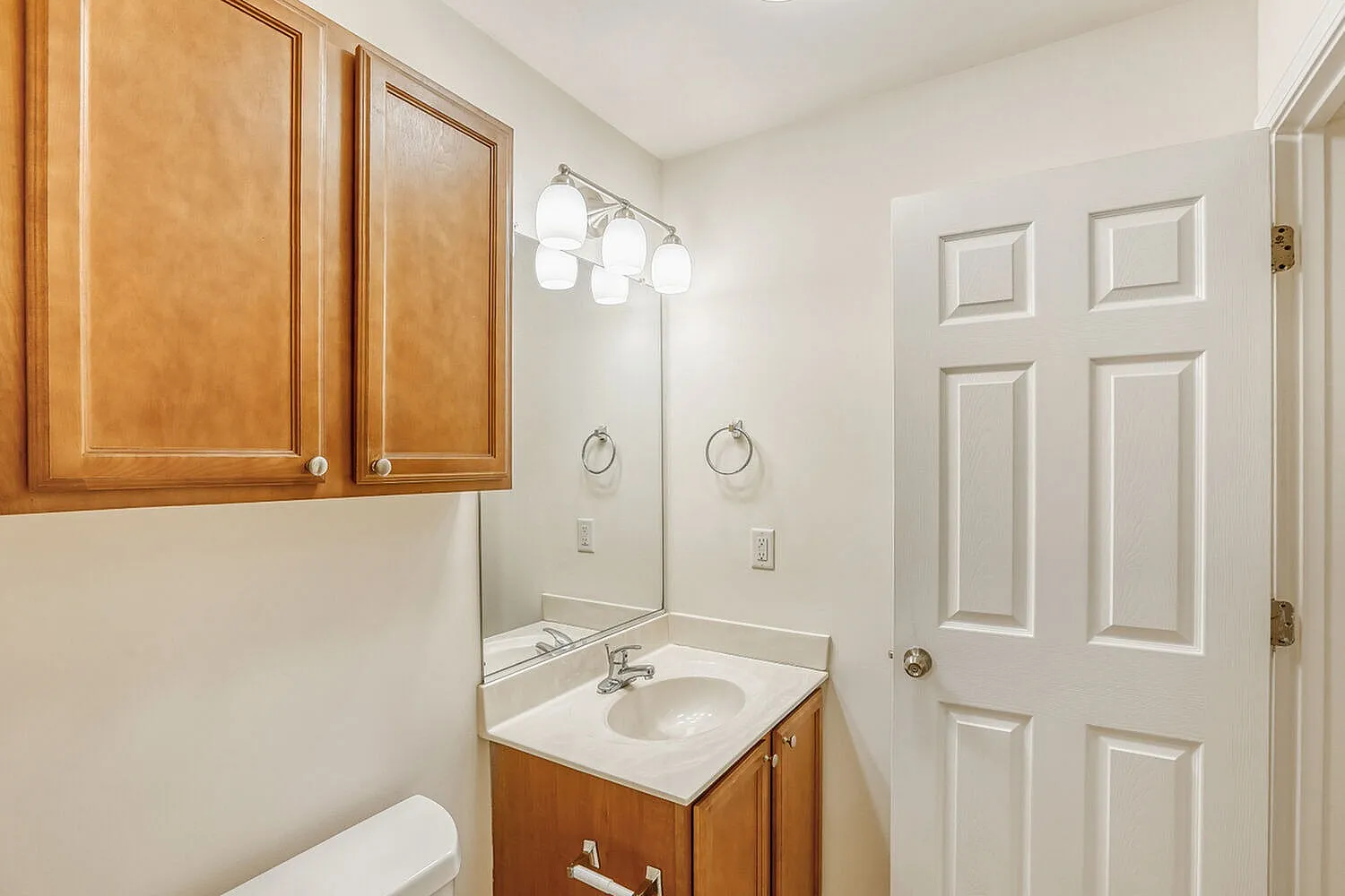 Bathroom, wood-style vanity cabinets, white sink countertop, mirror with pendant lighting